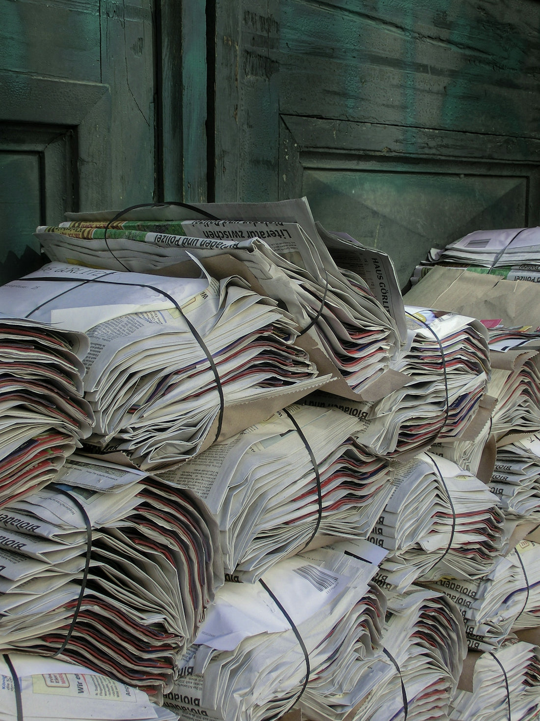 Stacks of bundled newspapers tied with black rubber bands against a green wooden door